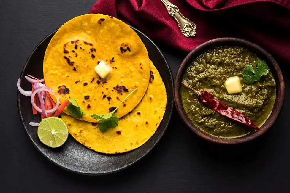 Sarson ka saag served with makki ki roti, onion, and lime